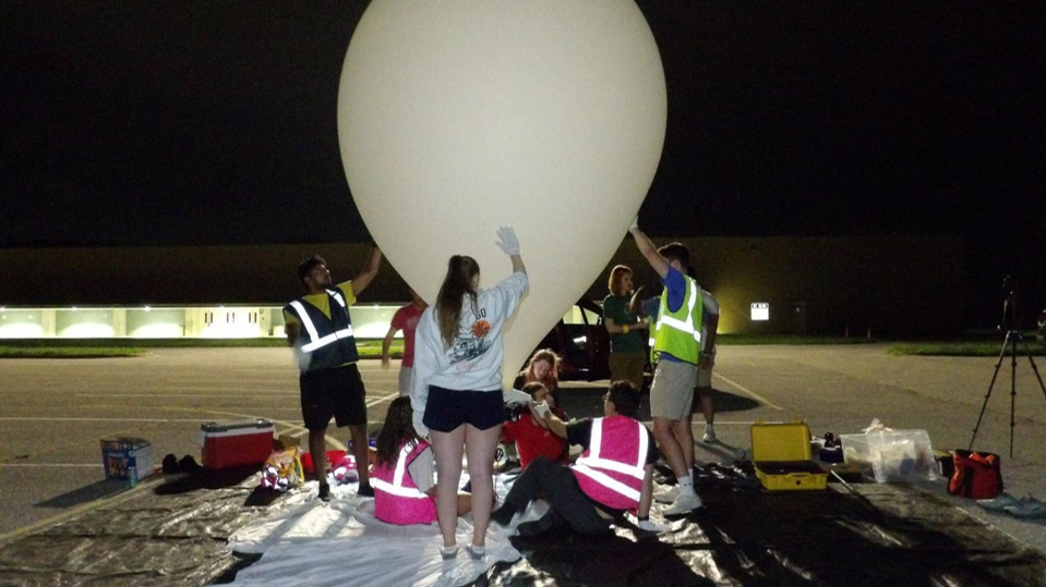 several students in safety vests around a balloon, preparing for launch
